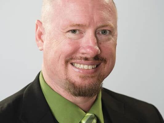 A professional portrait of James M Shaw in a green shirt and green tie