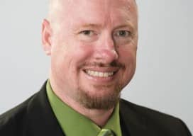 A professional portrait of James M Shaw in a green shirt and green tie