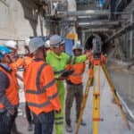 Working in the TBM access trench, a team uses a total station and handheld controller for automated measurement and data analysis.